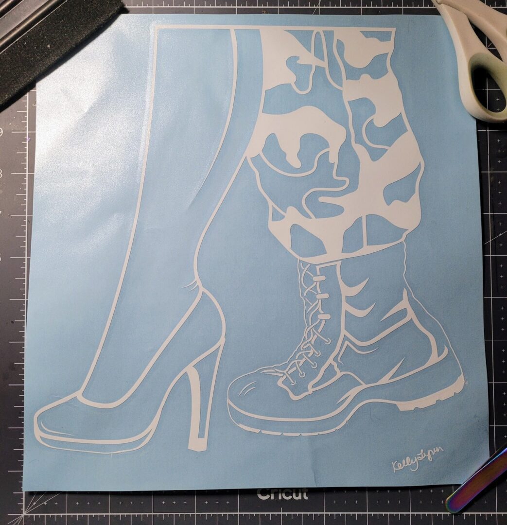The Transition" White Outline Window Decals of a high heel and a combat boot on a blue cutting mat with a pair of scissors on the side.