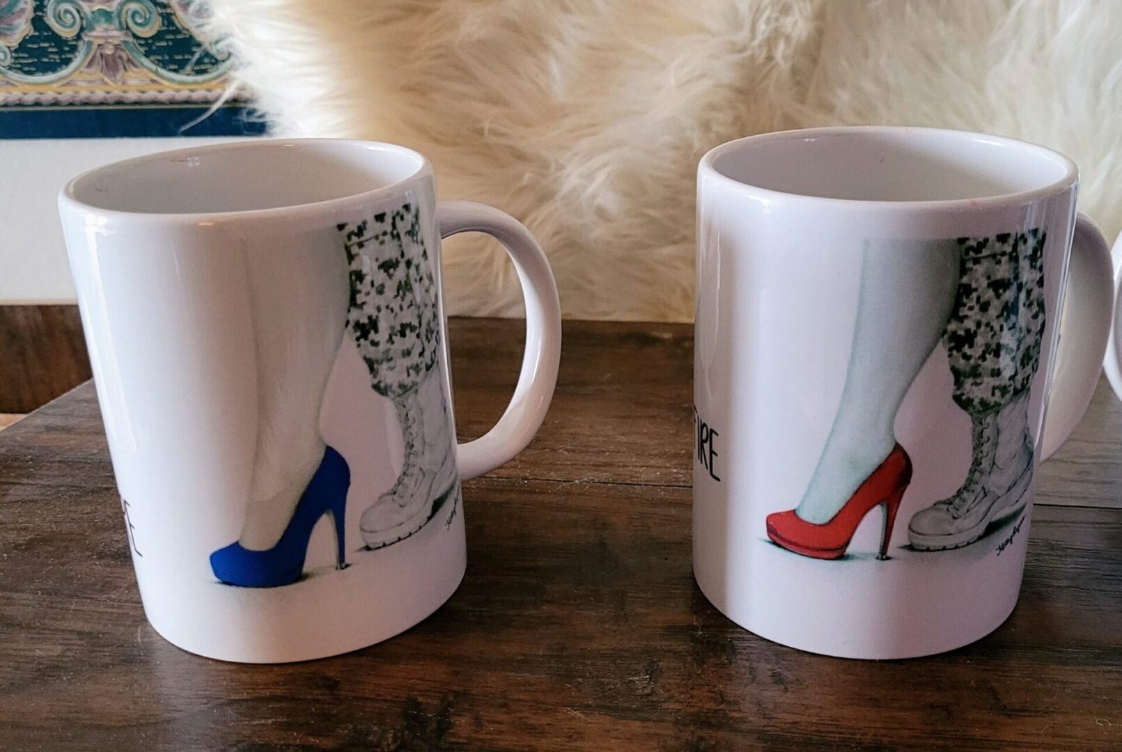 Two "The Transition" series 15 Oz Coffee Mugs on a wooden table, each featuring a graphic of a woman's legs wearing different colored high heels, one blue and one red.