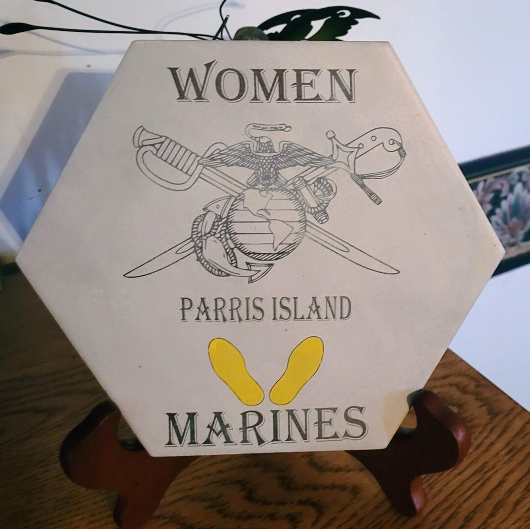 Hexagonal plaque with "women parris island marines" and an emblem, displayed on a wooden stand.