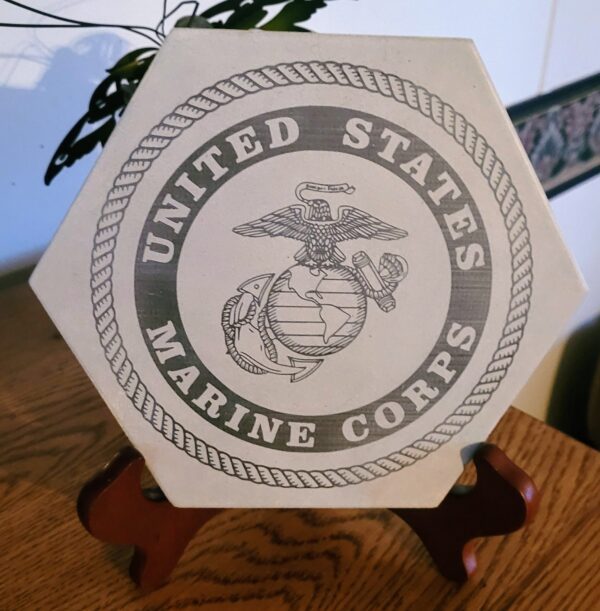Sentence with new product name: Military Themed Engraved Decorative Tiles displaying the united states marine corps emblem, standing on a wooden holder.