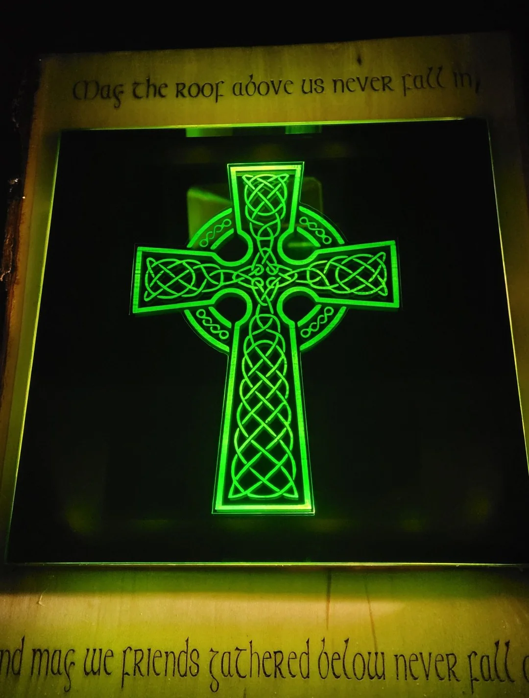 A Custom Engraved Mirrors celtic cross illuminates a sign with the inscription, "may the roof above us never fall in, and may the friends gathered below never fall out.