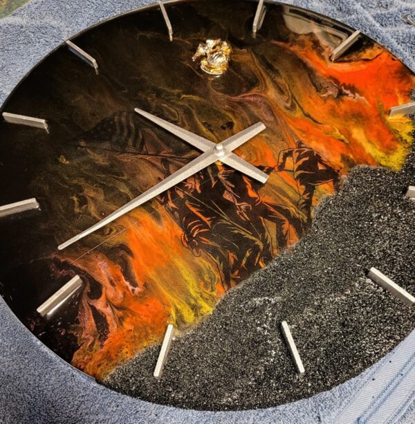 A Iwo Jima Resin Clock with an artistic representation of flames and sparkly black areas on its face, showing metallic hands and hour markers.