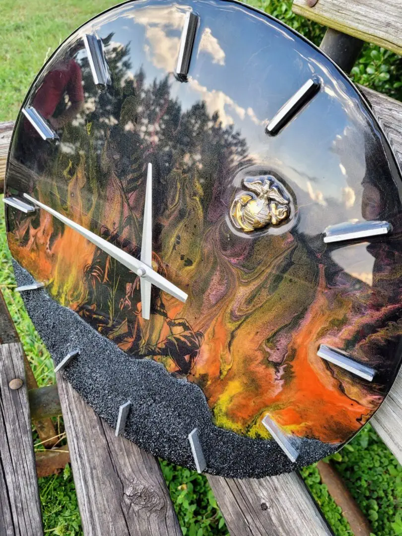 A Iwo Jima Resin Clock with an abstract, fiery landscape design and metal hour marks, photographed on a wooden surface outdoors.