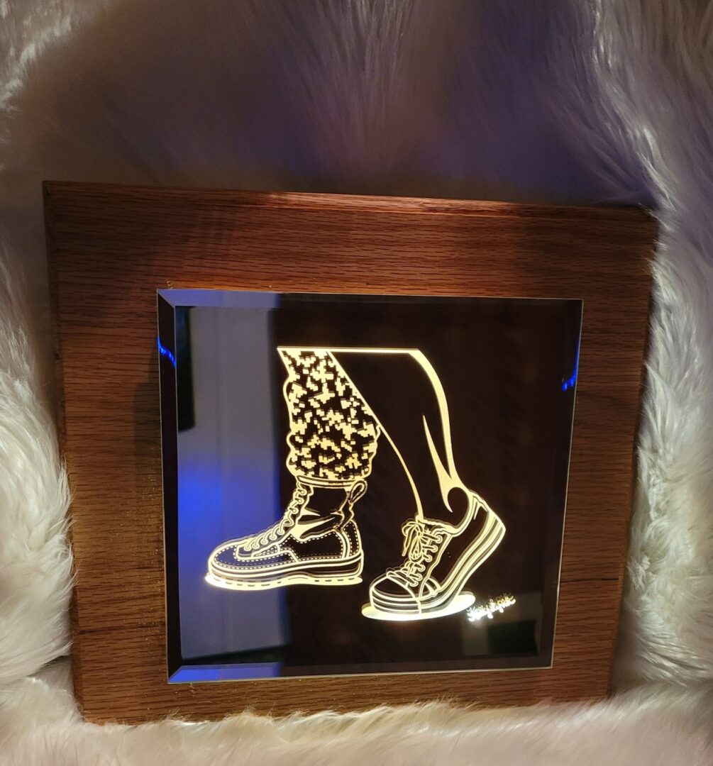 Lighted Mirror -Kelly McCook depicting a pair of lace-up boots, framed in wood and displayed against a white furry background.