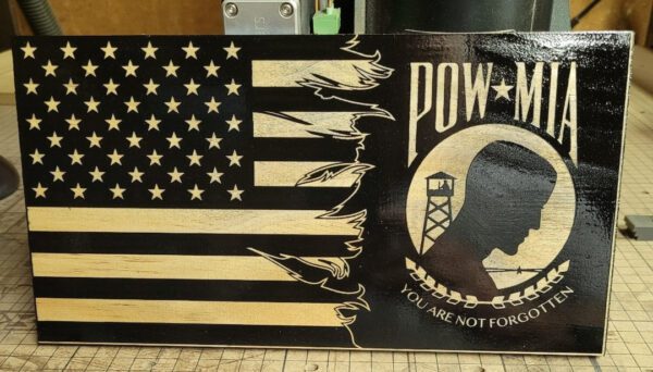 An American flag painted on a surface with alternating black and wood-stripe design, including a pow-mia emblem stating "you are not forgotten.
