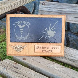 Commemorative bookshelf plaque on a wooden bench honoring ssgt daniel hammer, featuring military insignia and dates 1992-1997.