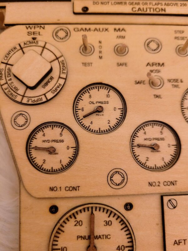 Close-up of a wooden panel with Legend Plaques engraved labels and dials, depicting various aircraft system controls like "hyd press" and "oil press".