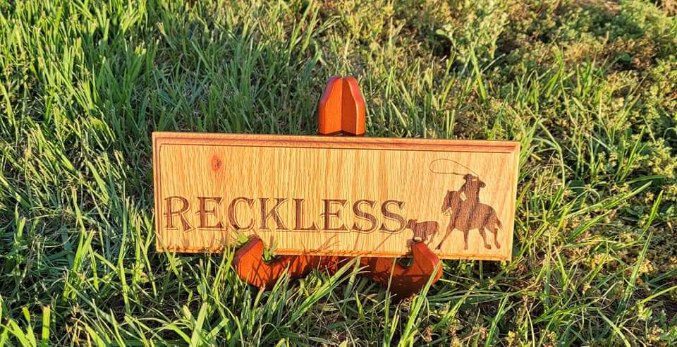 A wooden sign that says reckless with horses and a rider.
